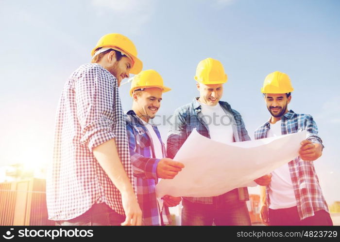 business, building, teamwork and people concept - group of smiling builders in hardhats with blueprint outdoors