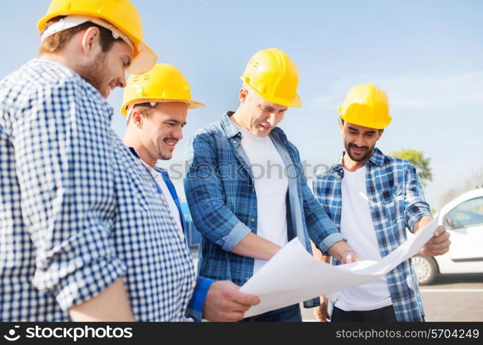 business, building, teamwork and people concept - group of smiling builders in hardhats with blueprint outdoors