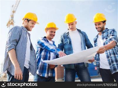 business, building, teamwork and people concept - group of smiling builders in hardhats with blueprint outdoors