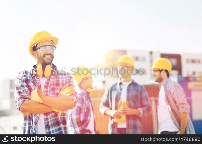 business, building, teamwork and people concept - group of smiling builders in hardhats with clipboard outdoors