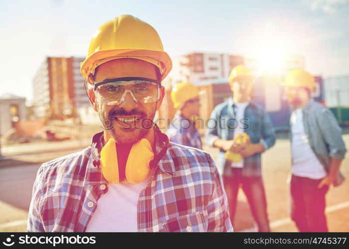 business, building, teamwork and people concept - smiling builder with hardhat and headphones over group of smiling builders at construction site