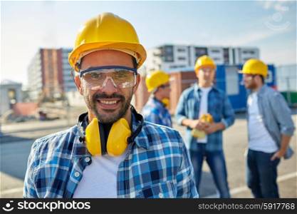 business, building, teamwork and people concept - smiling builder with hardhat and headphones over group of smiling builders at construction site
