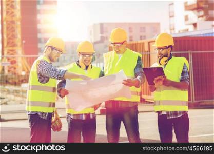 business, building, teamwork, construction and people concept - group of smiling builders in hardhats with blueprint and clipboard