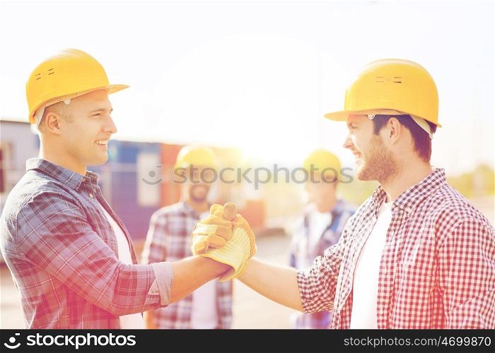 business, building, teamwork, gesture and people concept - group of smiling builders in hardhats greeting each other with handshake outdoors