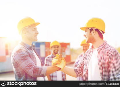 business, building, teamwork, gesture and people concept - group of smiling builders in hardhats greeting each other with handshake outdoors