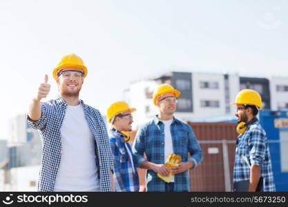 business, building, teamwork, gesture and people concept - group of smiling builders in hardhats showing thumbs up outdoors