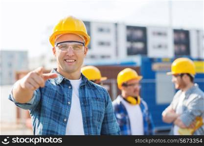 business, building, teamwork, gesture and people concept - group of smiling builders in hardhats pointing finger on you outdoors