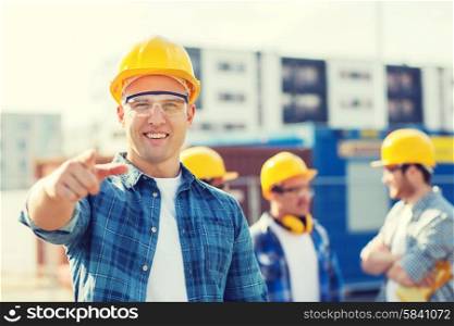 business, building, teamwork, gesture and people concept - group of smiling builders in hardhats pointing finger on you outdoors
