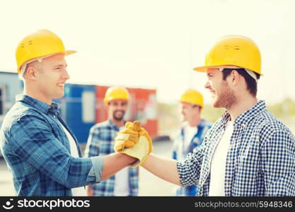 business, building, teamwork, gesture and people concept - group of smiling builders in hardhats greeting each other with handshake outdoors