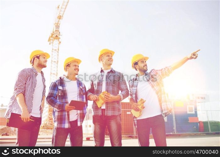 business, building, teamwork, technology and people concept - group of smiling builders in hardhats with tablet pc computer and clipboard outdoors