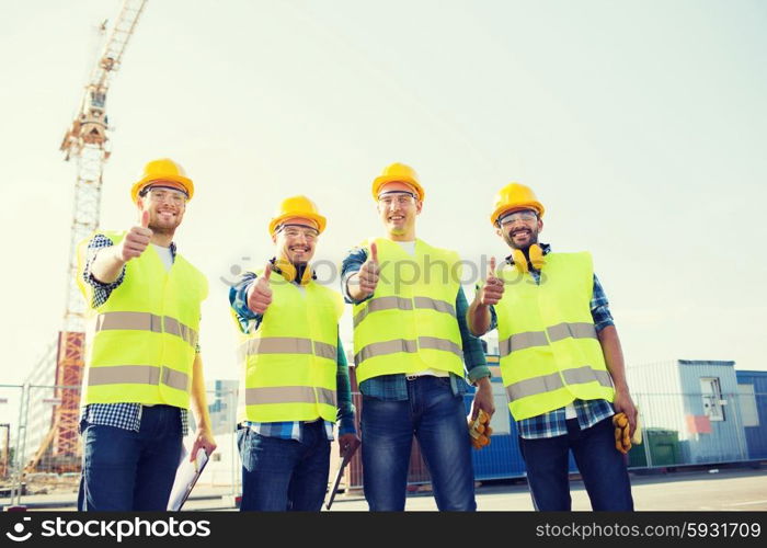 business, building, teamwork, technology and people concept - group of smiling builders in hardhats with tablet pc computer and clipboard showing thumbs up gesture outdoors