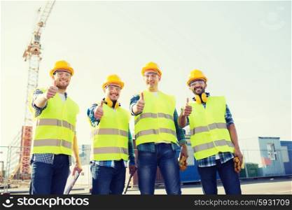 business, building, teamwork, technology and people concept - group of smiling builders in hardhats with tablet pc computer and clipboard showing thumbs up gesture outdoors