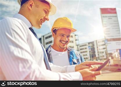 business, building, teamwork, technology and people concept - smiling builders in hardhats with tablet pc computer at construction