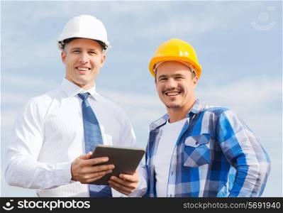 business, building, teamwork, technology and people concept - smiling builders in hardhats with tablet pc computer outdoors