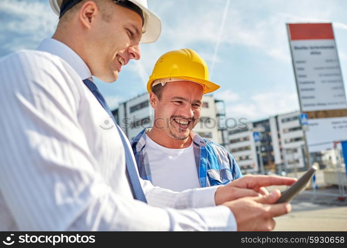 business, building, teamwork, technology and people concept - smiling builders in hardhats with tablet pc computer at construction