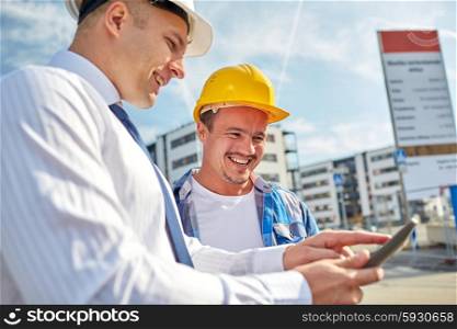 business, building, teamwork, technology and people concept - smiling builders in hardhats with tablet pc computer at construction
