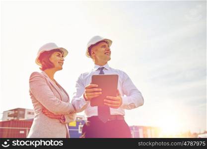 business, building, teamwork, technology and people concept - smiling man and woman in hardhats with tablet pc computer at construction site