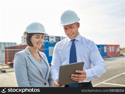 business, building, teamwork, technology and people concept - smiling man and woman in hardhats with tablet pc computer at construction site