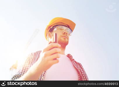business, building, technology and people concept - builder in hardhat with radio outdoors