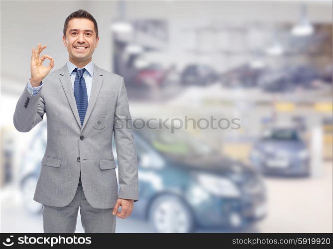 business, car sale, consumerism and people concept - happy man over auto show or salon background