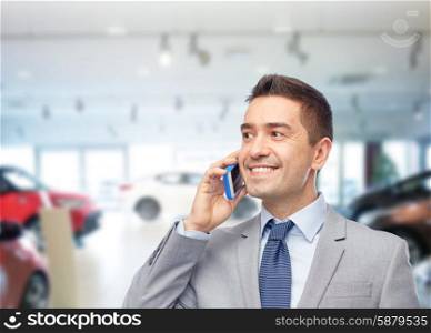 business, car sale, people and technology concept -happy businessman calling on smartphone over auto show or salon background
