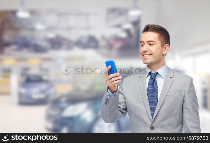 business, car sale, people and technology concept -happy businessman texting on smartphone over auto show or salon background