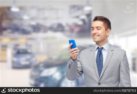business, car sale, people and technology concept -happy businessman texting on smartphone over auto show or salon background