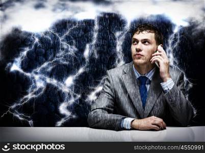 Business challenge. Young frustrated businessman under rain talking on mobile phone