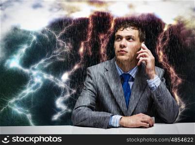 Business challenge. Young frustrated businessman under rain talking on mobile phone