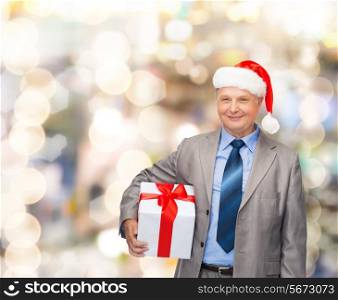 business, christmas, presents and people concept - smiling senior man in suit and santa helper hat with gift over lights background