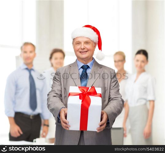 business, christmas, xmas, happiness concept - smiling old man in suit and santa helper hat with gift