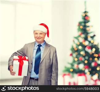 business, christmas, xmas, happiness concept - smiling old man in suit and santa helper hat with gift
