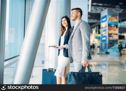 Business class passengers with baggage in airport, back view. Businessman and businesswoman in air terminal, negotiation trip