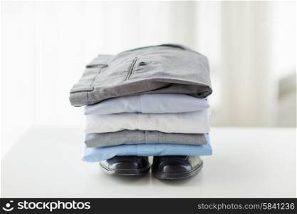 business, clothes, housekeeping and objects concept - close up of ironed and folded shirts, trousers and formal shoes on table at home