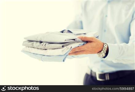 business, clothing and people concept - close up of businessman holding folded shirts
