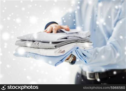 business, clothing and people concept - close up of businessman holding folded shirts over snow effect