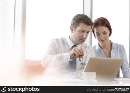 Business colleagues discussing over laptop while sitting in boardroom at office