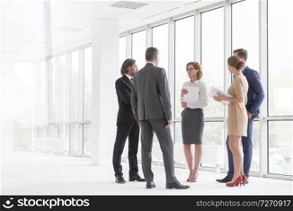 Business colleagues discussing while standing against window in new office