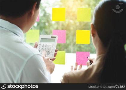 business collesgues using post it notes on glass wall calculating and discussing at modern office