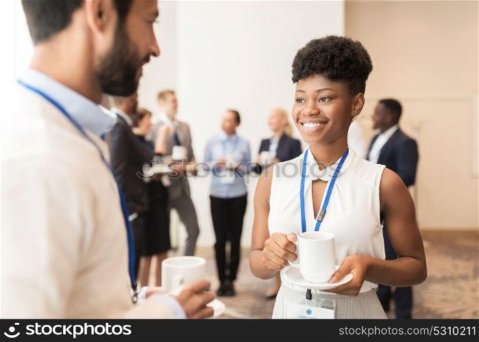 business, communication and education concept - international group of people with conference badges drinking coffee and talking at brake. business people with conference badges and coffee