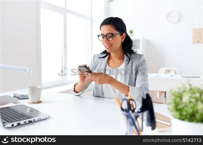 business, communication and people concept - happy businesswoman or secretary messaging on smartphone at office. businesswoman messaging on smartphone at office