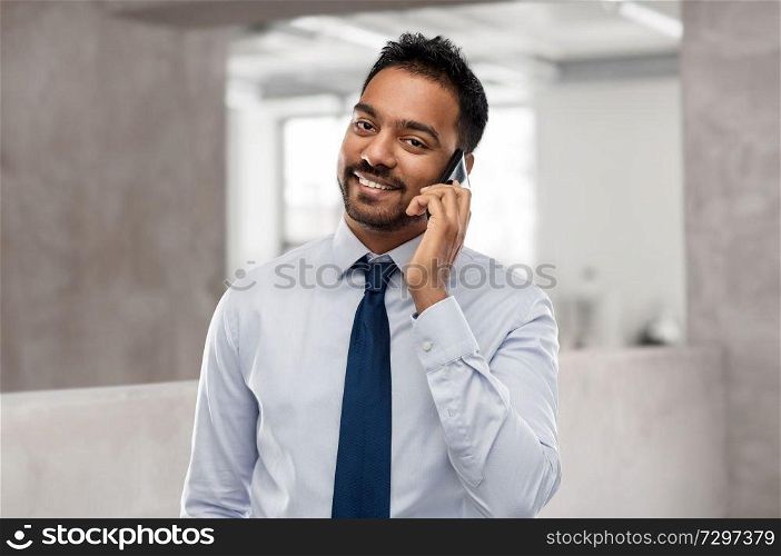business, communication and people concept - smiling indian businessman calling on smartphone over office background. indian businessman calling on smartphone at office