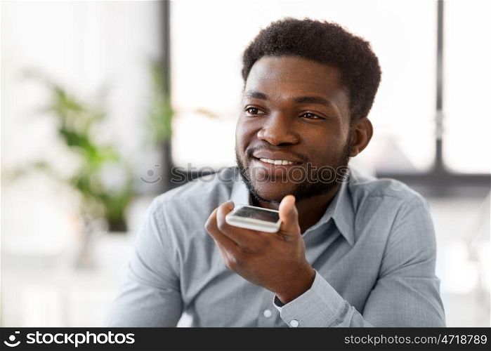 business, communication and technology concept - african american businessman calling or using voice recorder on smartphone at office. businessman records voice by smartphone at office. businessman records voice by smartphone at office
