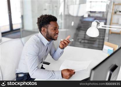 business, communication and technology concept - african american businessman with papers calling or using voice recorder on smartphone at office. businessman records voice by smartphone at office. businessman records voice by smartphone at office