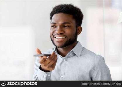 business, communication and technology concept - african american businessmanr calling or using voice recorder on smartphone at office. businessman records voice by smartphone at office. businessman records voice by smartphone at office