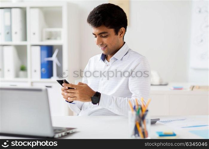 business, communication and technology concept - happy businessman messaging on smartphone at office. businessman messaging on smartphone at office