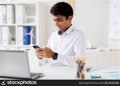 business, communication and technology concept - happy businessman messaging on smartphone at office. businessman messaging on smartphone at office