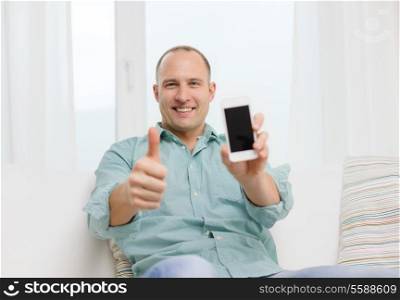 business, communication, home and modern technology concept - smiling man with smartphone at home showing thumbs up