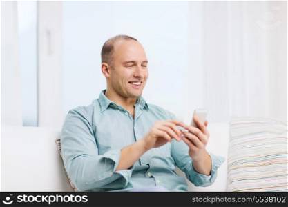 business, communication, home and modern technology concept - smiling man with smartphone at home
