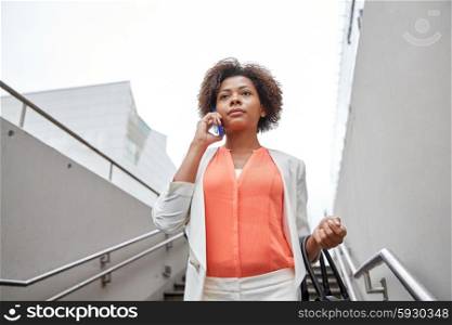 business, communication, technology and people concept - young african american businesswoman calling on smartphone going down stairs into city underpass